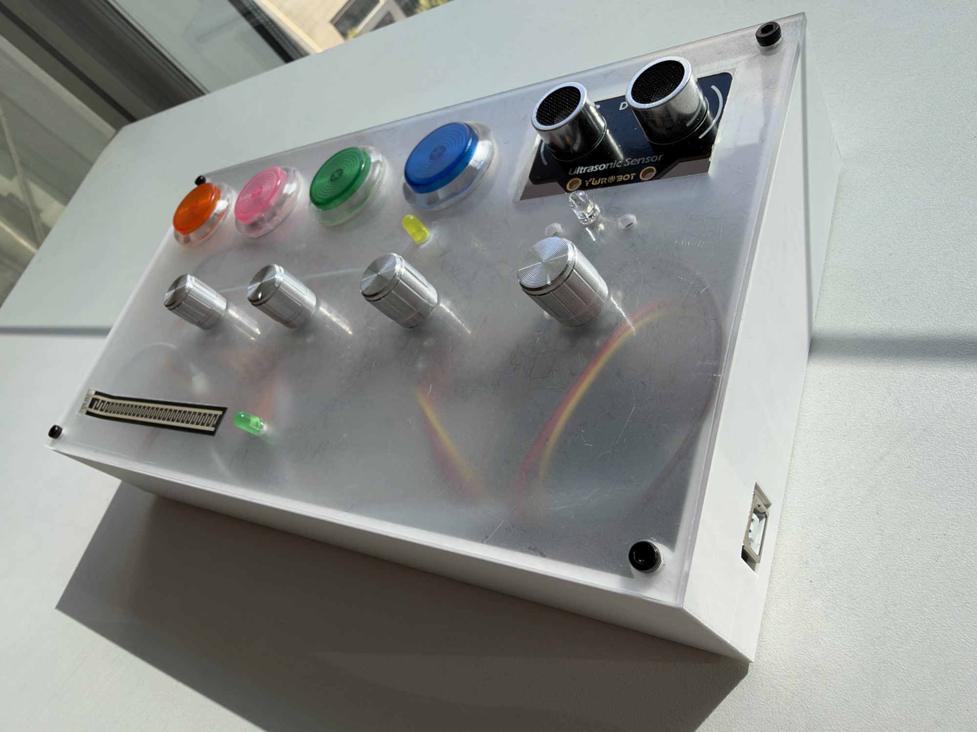 Chip Trigger controller: a frosted acrylic panel with four coloured arcade buttons, four silver knobs, a pressure strip and an ultrasonic sensor, set in a white enclosure.