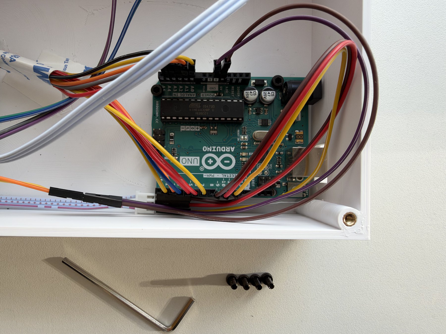 Interior of the white enclosure with an Arduino Uno, bundled colour-coded wiring, a ribbon cable and the shell mounting posts.